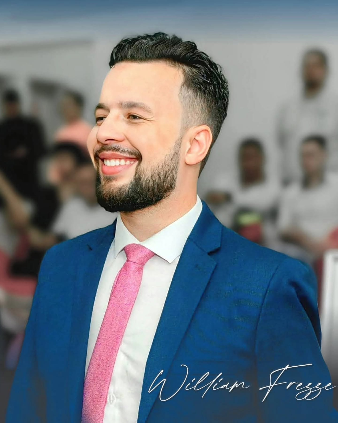 William Frezze sorrindo em um evento, com terno azul, camisa branca e gravata rosa